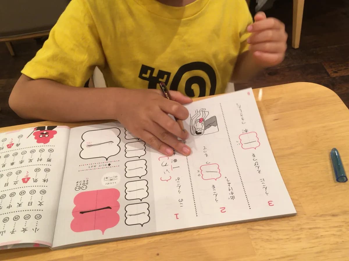 A child writing kanji in a practice drill book