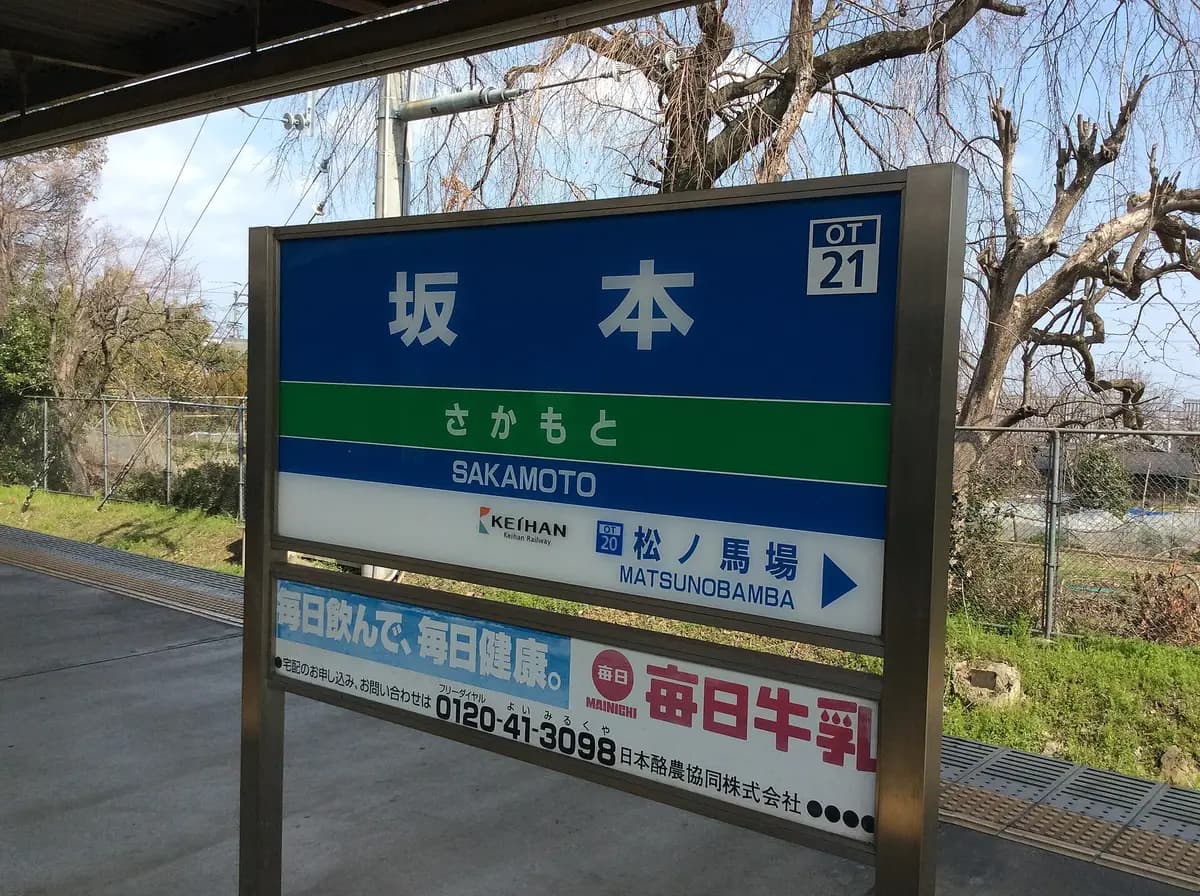 A train station sign reading 坂本 in kanji, さかもと in hiragana and SAKAMOTO in romaji
